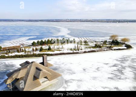 Inverno bellissimo paesaggio con un fiume ghiacciato e piccole case con tetti di canna sull'isola. Stile rustico, tetto di paglia, gabbia. Foto aerea drone vi Foto Stock