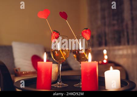 Festa di San Valentino a casa con bicchieri da vino champagne con fragole in cima circondato da candele Foto Stock