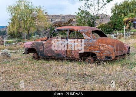 Una vecchia auto arrugginita senza finestre o pneumatici abbandonata in un campo Foto Stock
