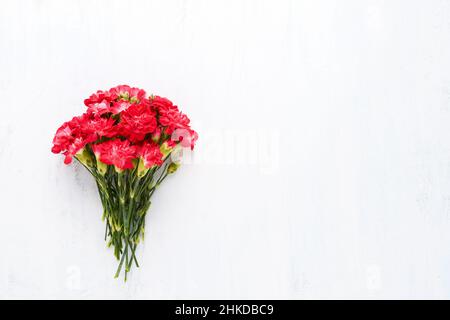 Bouquet di fiori di garofano rosso su sfondo bianco di legno. Festa della mamma, giorno di San Valentino, concetto di festa di compleanno. Disposizione piatta, spazio di copia per il testo Foto Stock