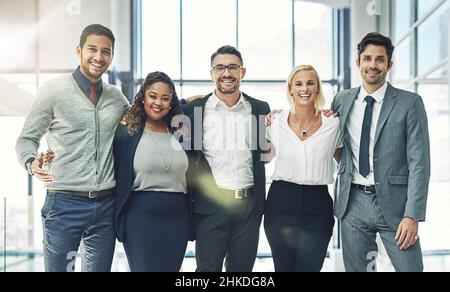 Il nostro team non conosce limiti. Ritratto di un gruppo diversificato di colleghi sorridenti in piedi braccio in un ufficio. Foto Stock