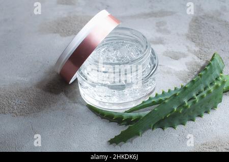 Struttura in gel con bolle di acido ialuronico e rami di aloe vera in un vaso di vetro su sfondo concreto Foto Stock