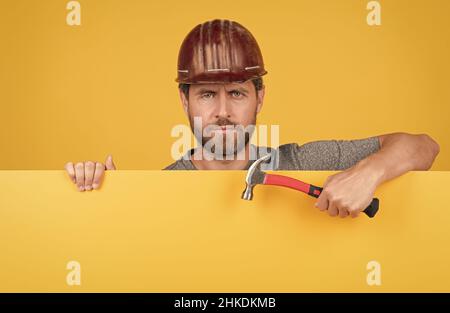 operaio sopportato in hardhat dietro foglio di carta giallo. annuncio del lavoratore di pubblicità Foto Stock