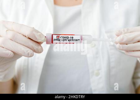 Testo positivo Omicron sulla provetta per campioni di sangue positiva con la nuova scheda Omicron Variant covid 19 nelle mani del medico in camice bianco e guanti Foto Stock