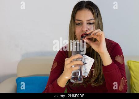 Bella ragazza bionda sensazione di male e prendere pillole mentre trascorrere il tempo a casa. La ragazza depressa tiene il antidolorifico per il dolore mestruale. Foto Stock