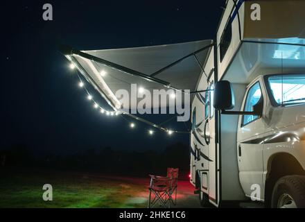 Tempo di vacanza accogliente Campground. Modern Class C Motorhome RV con luci a corda sulla tenda del camperino. Tema veicoli da diporto. Foto Stock