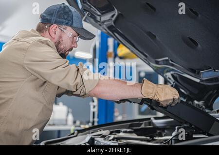 Caucasian Professional Car Mechanic nel suo 30s esecuzione di manutenzione moderna del veicolo. Controllo degli elementi e dei sistemi del motore sotto il cofano del veicolo. Trasporto Foto Stock