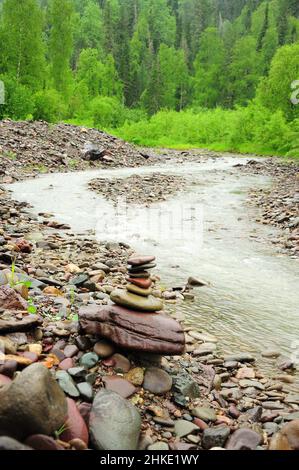 Una piccola piramide di pietre sulla riva tortuosa di un piccolo fiume di montagna che scorre attraverso la foresta mattutina dopo la pioggia. Fiume Iogach, Altai, Siberia, R. Foto Stock