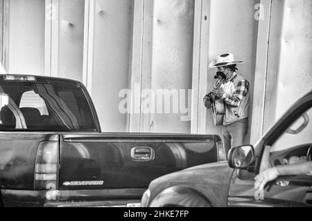 Un'immagine in bianco e nero di un uomo che usa i suoi talenti musicali sulla chitarra per fare alcuni pesos e mantenere la sua famiglia nutrita. Foto Stock