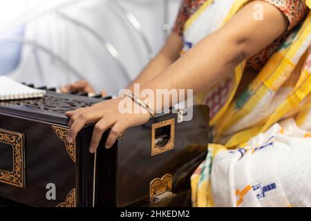 Una donna indiana in saree che canta e suona l'armonio su sfondo bianco Foto Stock