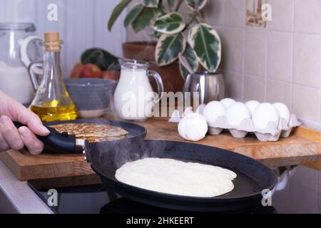 Casalinga donna frittelle pancake per la prima colazione. Home cottura frittelle in padella su vetroceramica in cucina. FAI DA TE. Ingredienti per preparare pancake Foto Stock
