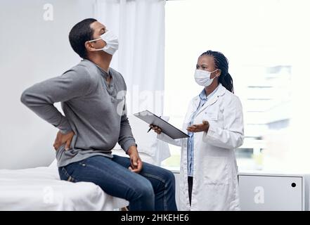 Quali altri sintomi ha avuto. Shot di un medico che ha una consultazione con un paziente che soffre di mal di schiena. Foto Stock