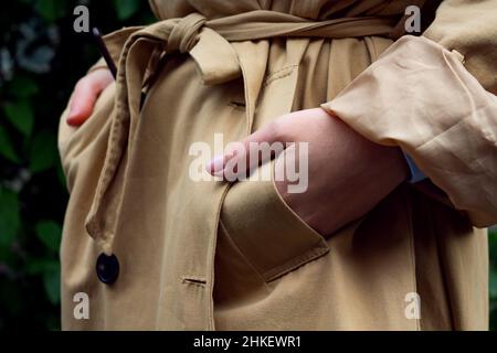 Mani in tasche di trench beige. Foto Stock