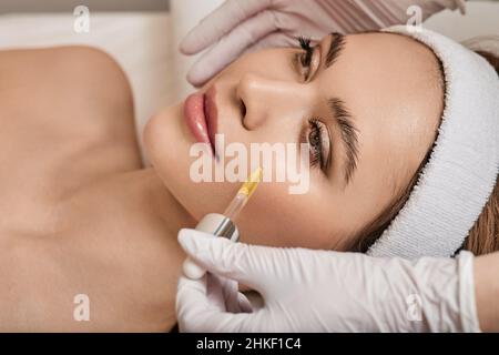 cura della pelle del viso con olio cosmetico e siero per il trattamento. Bella donna mentre l'estetista le applica il siero sul viso nel salone di bellezza Foto Stock