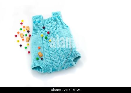 Abito a maglia manuale per un neonato con motivo Aran, aghi da maglieria, dolci e orsi su sfondo bianco. Posiziona per testo. Denaro lavorato a maglia blu bambino Foto Stock