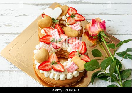 Pan di Spagna con fragole, barrette di cioccolato rosa, crema alla vaniglia e biscotti con colza di cuore a forma di numero 8 con rosa rosa. Un regalo speciale Foto Stock