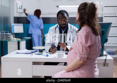 Medico afroamericano che dà una bottiglia di pillole a donna incinta per curare la malattia. Pallone di tenuta per specialisti con medicinale da prescrizione e trattamento da somministrare al paziente in attesa di un bambino. Foto Stock