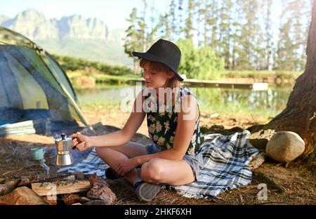 Caffè del mattino sulla birra. Shot di una giovane donna che fa il caffè su un fuoco aperto in un campeggio. Foto Stock