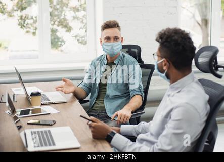 Gli uomini d'affari hanno discussioni che indossano maschere protettive mediche, colleghi che lavorano in ufficio. Cura di sé, stile di vita aziendale, protezione da coronavirus Foto Stock