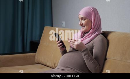 Donna incinta in hijab controlla il numero e fa una telefonata Foto Stock