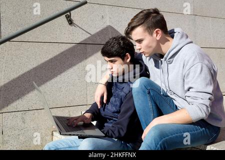 vista laterale due ragazzi gay seduti su una scala utilizzando un computer portatile Foto Stock