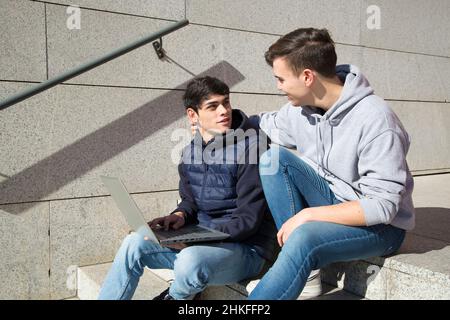 due ragazzi gay che si siedono su una scala usando un computer portatile che si guardano e parlano Foto Stock