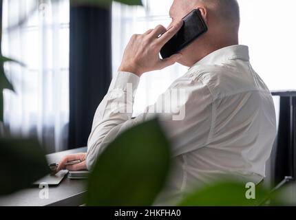 Uomo d'affari maturo seduto alla scrivania con computer portatile e pianificatore. Dipendente che lavora in ufficio e risponde alle chiamate telefoniche. Concetto di chiamata aziendale. Foto di alta qualità Foto Stock
