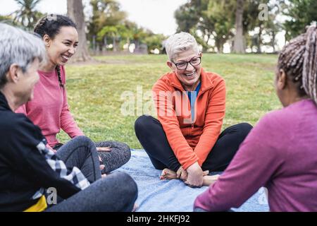 Happy donne multi generazionali divertirsi insieme seduti all'aperto al parco della città - Focus principale sulle braccia del centro senior femminile Foto Stock