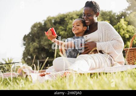 Felice madre incinta e figlio divertirsi a fare selfie al parco della città - Focus principale sul viso del ragazzo Foto Stock