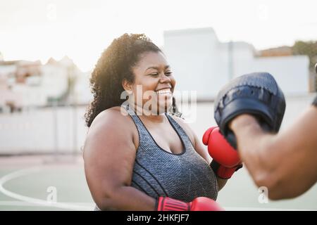 Donna curvy africana e personal trainer fare boxing sessione di allenamento all'aperto - concentrarsi sul viso Foto Stock