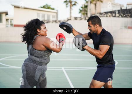 Donna curvy africana e personal trainer fare boxing sessione di allenamento all'aperto - fuoco sul guanto di destra di vettura Foto Stock