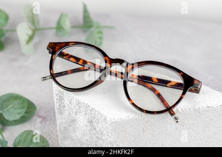 Occhiali eleganti su un podio in pietra naturale. Occhiali e piante di colore leopardo su sfondo di cemento Foto Stock
