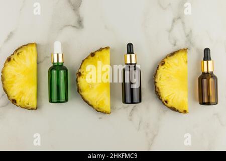 tre bottiglie diverse con pipetta e tre succose fette di ananas con olio di frutta su sfondo marmoreo. disposizione piatta. vista dall'alto Foto Stock