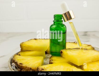 una bottiglia di vetro verde è appoggi su fette di ananas con un cosmetico riempito con una pipetta. cosmetici naturali idratanti Foto Stock