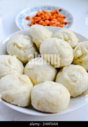 Panini al vapore cinesi, baozi, colazione popolare in Cina. Vegetariano sottaceto con peperoncino rosso sfocato sullo sfondo. Foto Stock