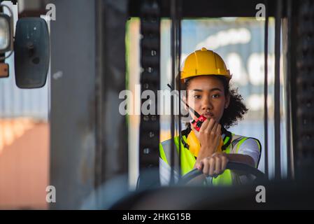 Il caposquadra femmina usa la comunicazione radio per comunicare mentre guida il carrello elevatore al deposito del contenitore di spedizione. Spedizione in banchine. Foto Stock