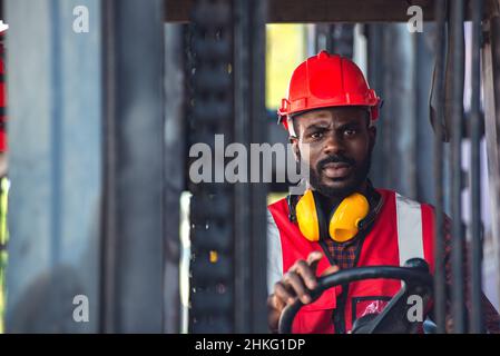 Lavoratore di sesso maschile in uniforme e casco che guida e funziona su carrello elevatore a forche con container diesel presso la banchina commerciale. Foto Stock