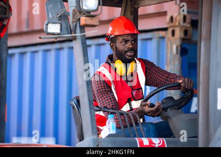 Lavoratore di sesso maschile in uniforme e casco che guida e funziona su carrello elevatore a forche con container diesel presso la banchina commerciale. Foto Stock