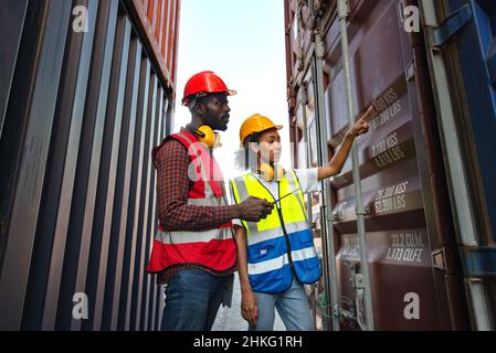 Due lavoratori afroamericani maschi e femmine controllano e controllano i container di carico della nave Cargo per l'esportazione all'importazione. Foto Stock