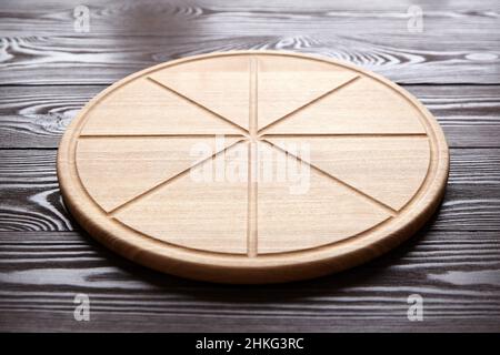 Tagliere rotondo per pizza con scanalature a fette su tavola di legno marrone Foto Stock