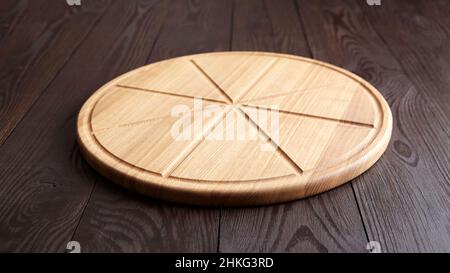 Tagliere rotondo per pizza con scanalature a fette su tavola di legno marrone Foto Stock