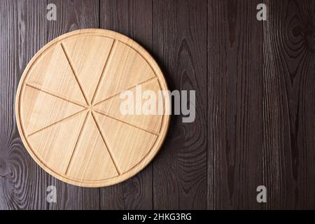 Tagliere rotondo per pizza con scanalature a fette su tavolo di legno marrone con vista dall'alto dello spazio per la copia Foto Stock