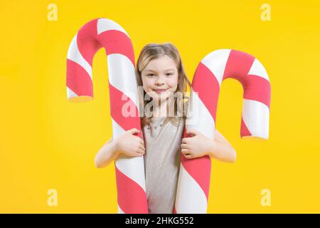 La ragazza adolescente carina abbraccia due caramelle enormi su uno sfondo giallo. Dolci di Natale. Lollipop. Buon preschooler con dolci in mano. Foto Stock