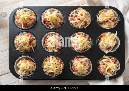 Vassoio da forno con muffin per pizza preparati e sostanziosi da pasta di lievito, pomodori, verdure, salsiccia e formaggio pronti per il forno, vista ad angolo alto da abo Foto Stock