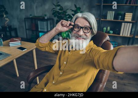 Autoritratto di attraente uomo dai capelli grigi e allegri esperto geek toccare le specifiche che posano al loft interno luogo di lavoro stazione al chiuso Foto Stock