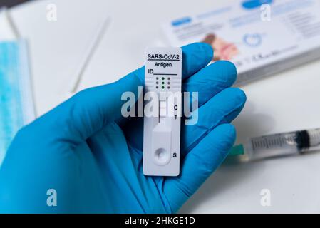 Una mano che indossa un guanto protettivo è vista che tiene un test rapido di Covid, anche noto come test dell'antigene o test di flusso laterale, che mostra un risultato positivo in un Foto Stock