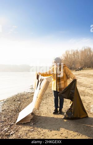 Una giovane donna che pulisce la spiaggia dai rifiuti di cartone Foto Stock