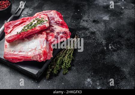 Costolette di manzo di vitello, sparerib crudo su tavola di marmo. Sfondo nero. Vista dall'alto. Spazio di copia Foto Stock