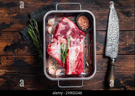 Costolette di manzo crudo in vassoio d'acciaio con rosmarino. Sfondo in legno. Vista dall'alto Foto Stock