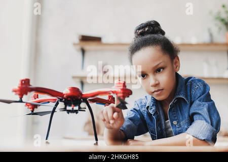 Giovane ragazza carina che tiene quadcopter. Bambino che gioca con drone a casa. Istruzione, studio domestico, bambini, tecnologia, scienza, futuro, concetto di persone Foto Stock